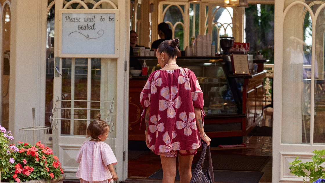 Women in maroon coloured set walking into a cafe with her toddler