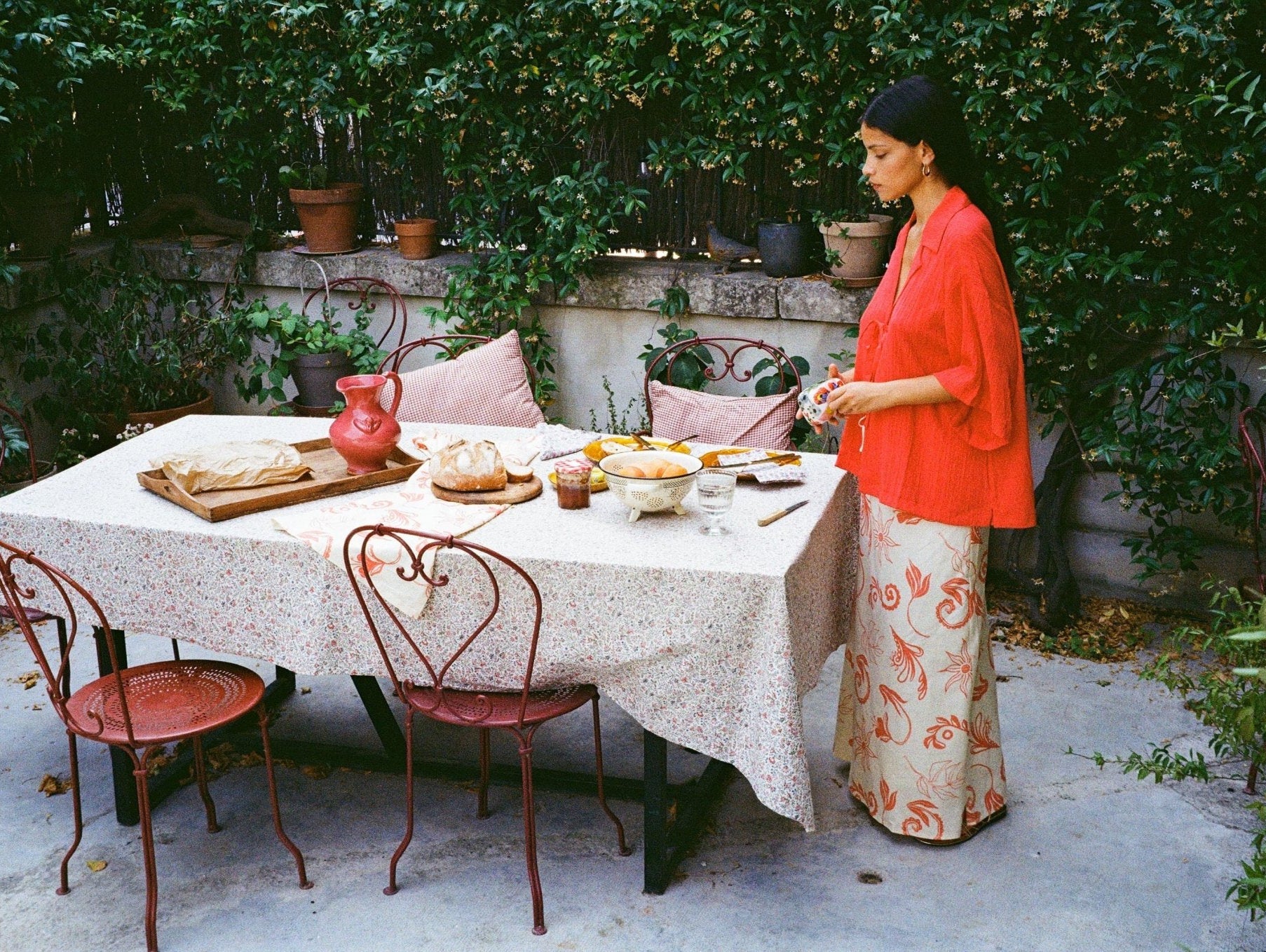 Women standing by outdoor table making lunch wearing a red shirt and printed maxi skirt