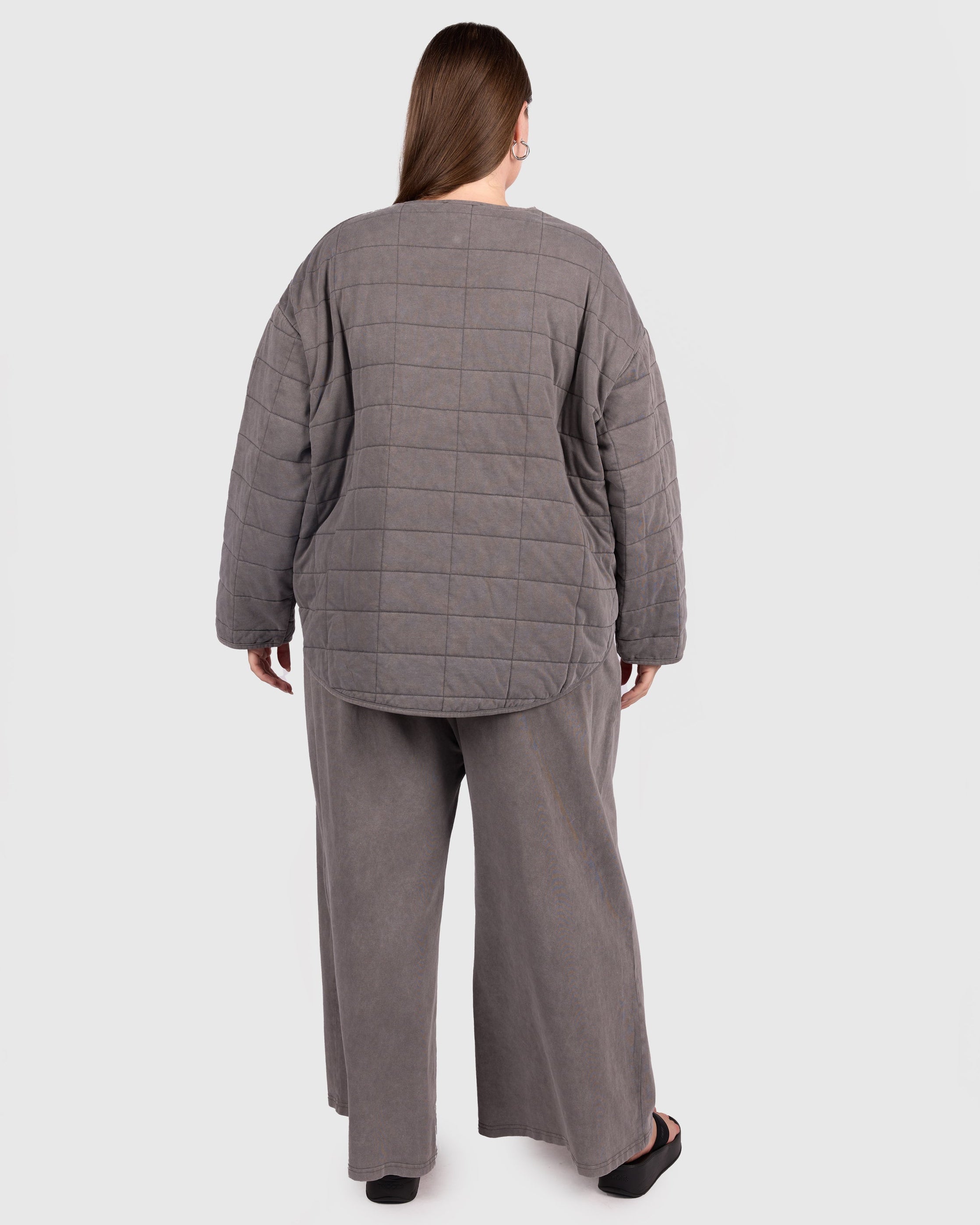 Person wearing a gray quilted jacket and pants on a white background