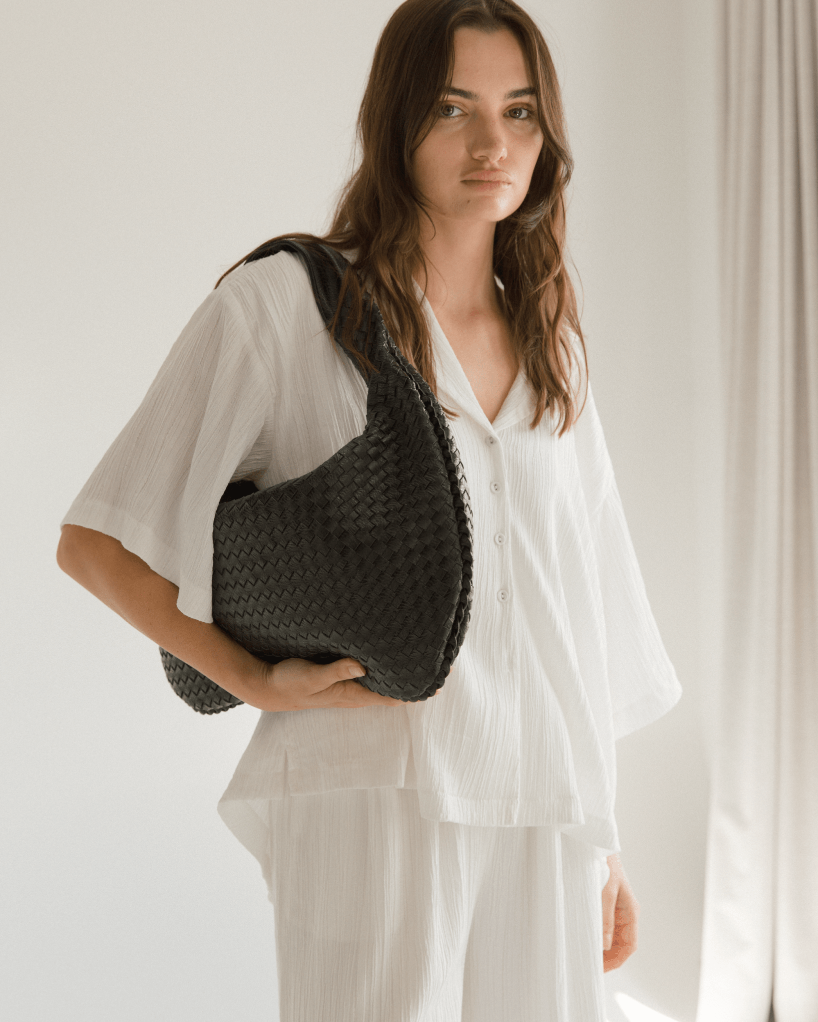 Woman holding a black woven handbag against a plain background