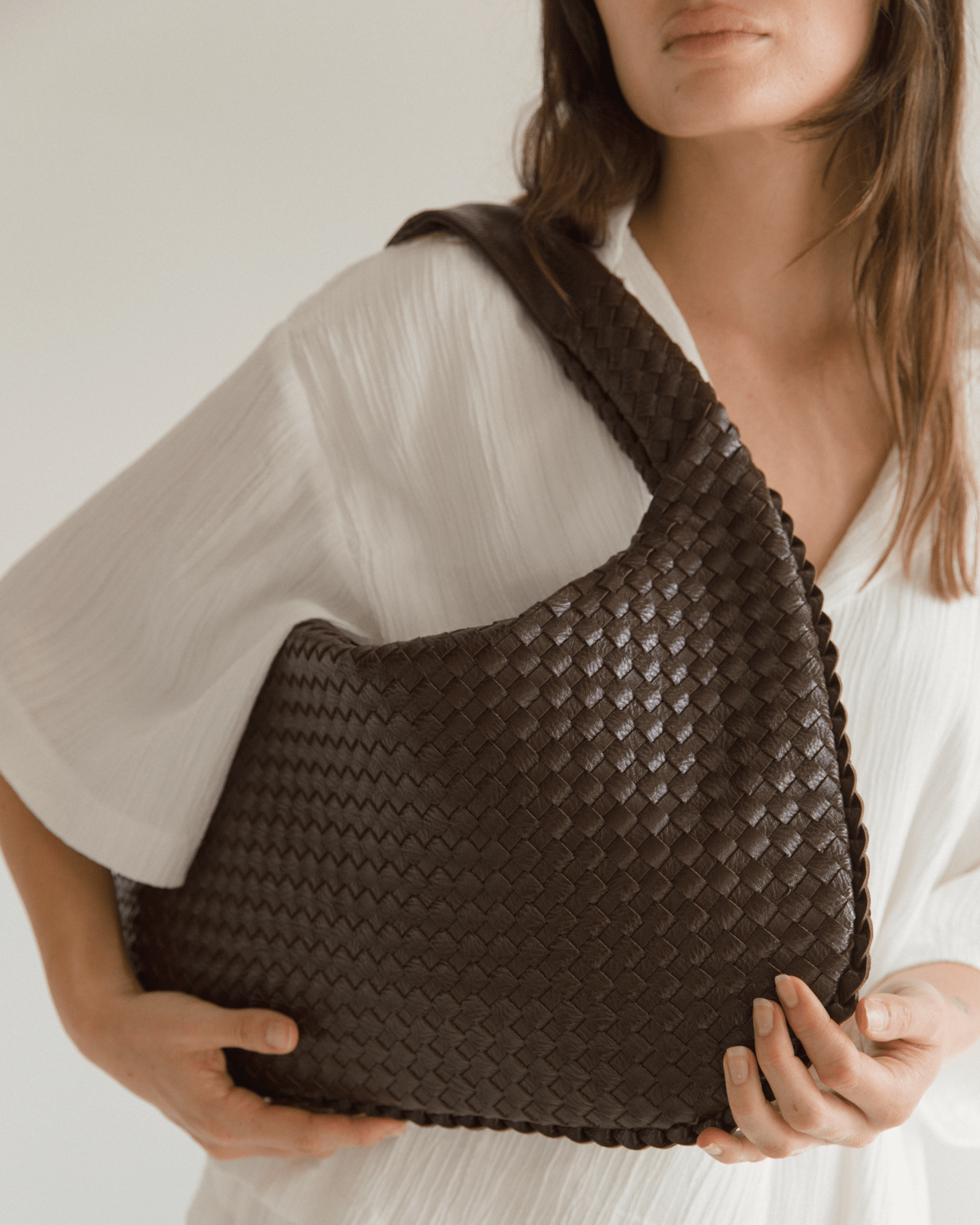 Person holding a brown woven handbag against a neutral background