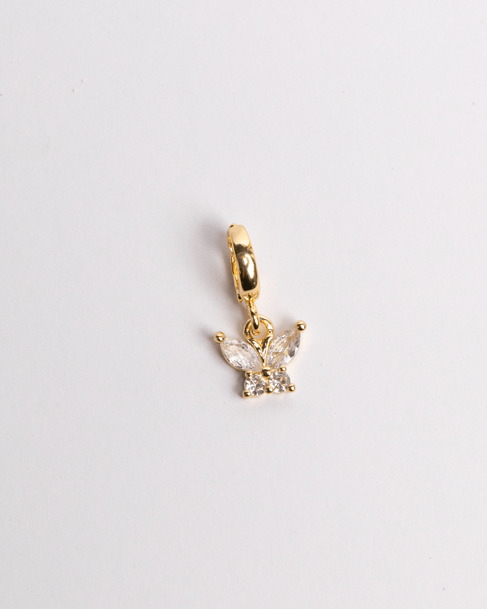 A gold-colored charm in the shape of a butterfly with crystal detailing