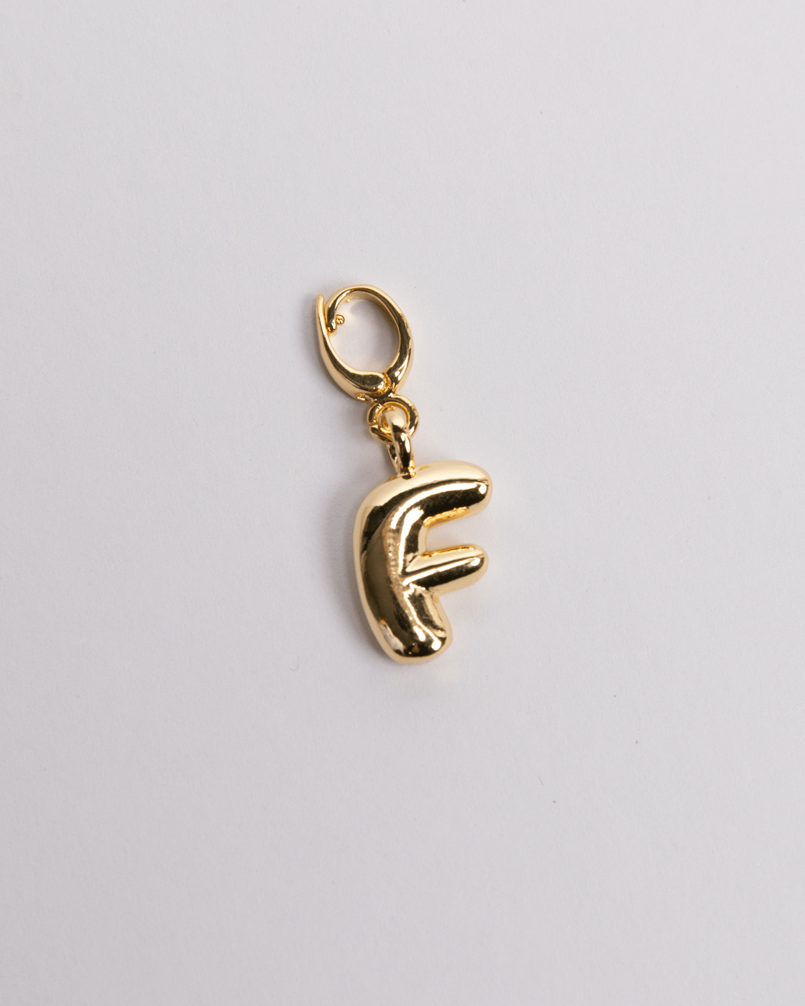 A gold-plated stainless steel charm in the shape of the letter 'F' with a clasp for attaching to jewelry.