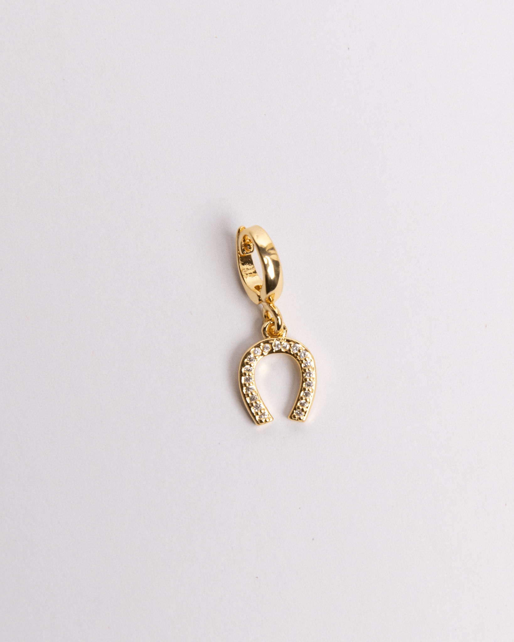 A gold-colored horseshoe-shaped charm with a clasp on one end, isolated on a white background.