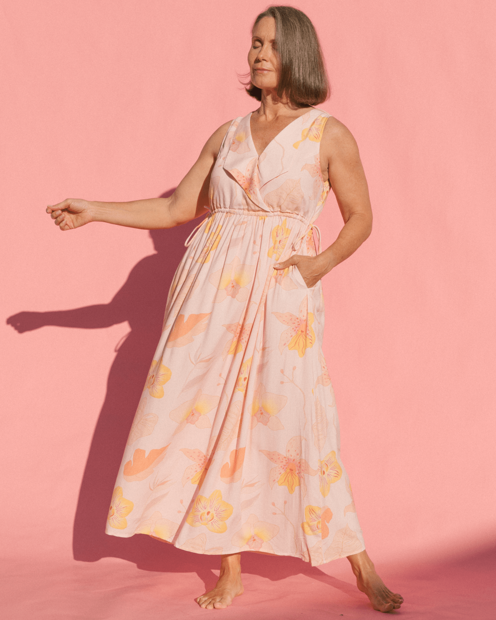 Woman wearing light pink floral dress with side pockets & adjustable drawstring waist.