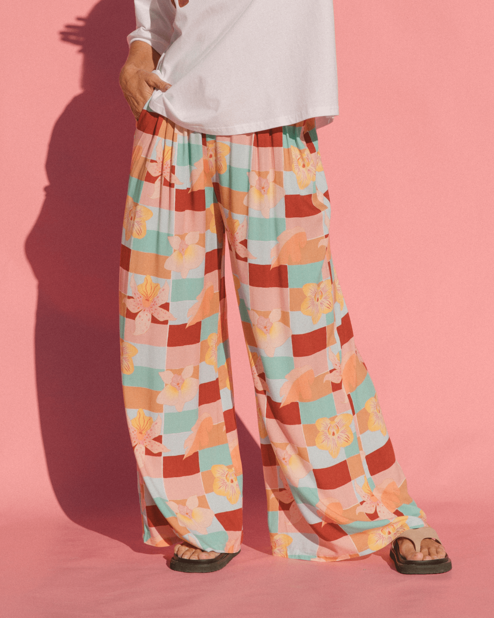 Woman wearing flowy & breathable wide legged pants in a geometric multicoloured checkered print.