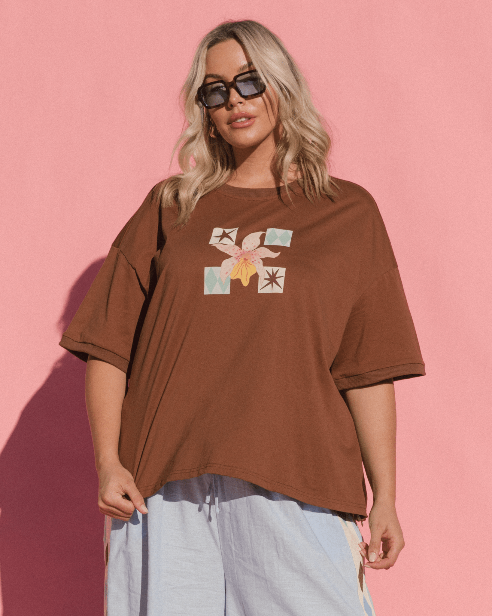 Woman wearing an oversized brown graphic tee with floral print and blue pants.