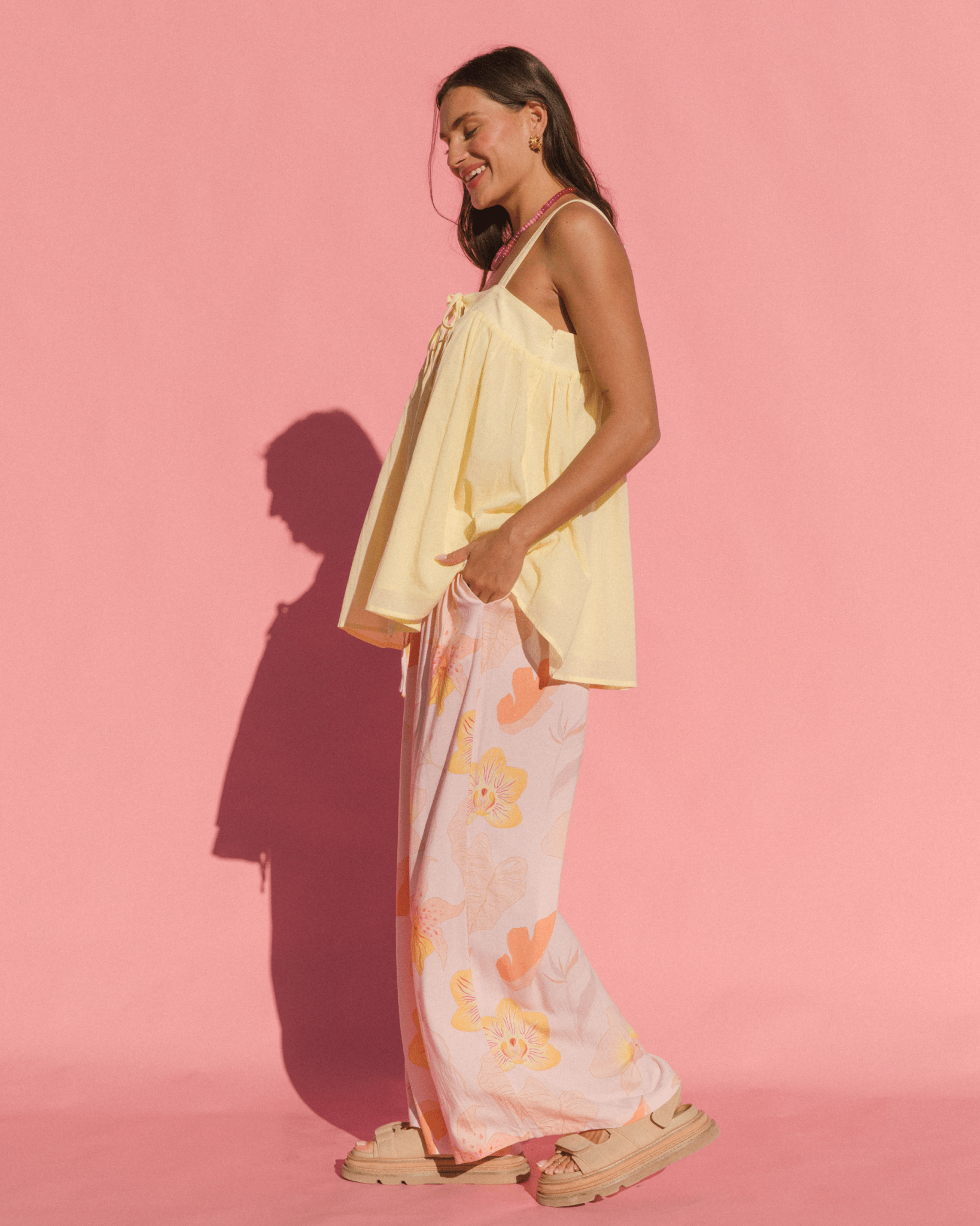 Woman wearing a yellow top and floral skirt against a pink background