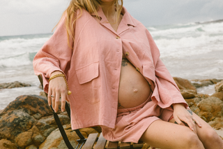 pregnant mother sitting on a chair at the beach showing her beautiful bump wearing loungewear