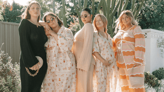 five women wearing crochet and lounge wear standing next to each other posing in a backyard