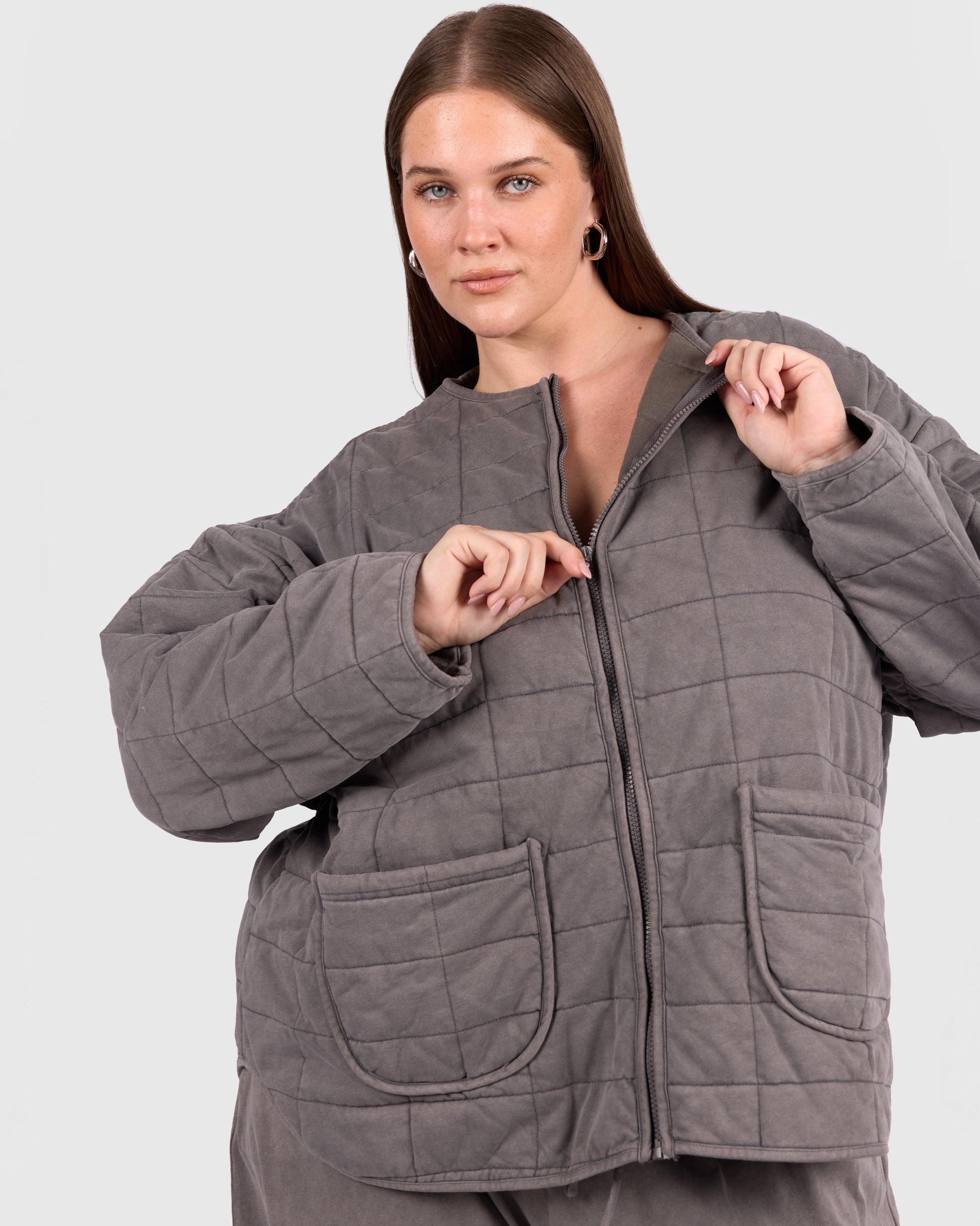 Woman wearing a warm charcoal quilted jacket with a zip and pockets. 
