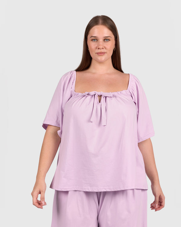 Woman wearing a light purple top and pants on a plain background