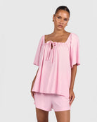 Woman wearing a pink top and shorts set on a light gray background