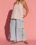 Woman wearing flowy pink strapless halter neck top with an adjustable neckline, paired with pale blue long lounge pants with diamond detailing. 