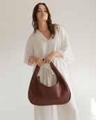 Woman holding a maroon woven handbag against a plain background
