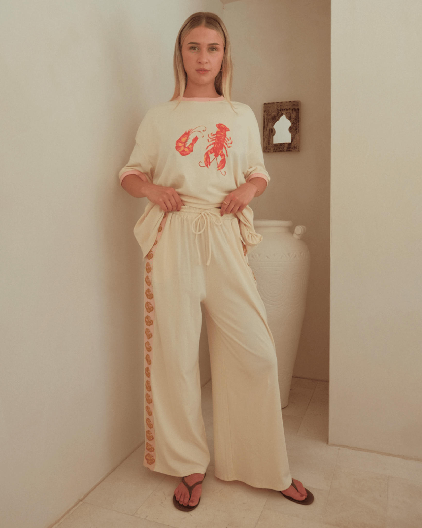 Woman wearing a cream-colored outfit with a red graphic design in a bathroom.