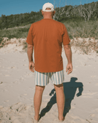 Man walking on a sandy beach wearing an relaxed fit shirt and striped shorts.