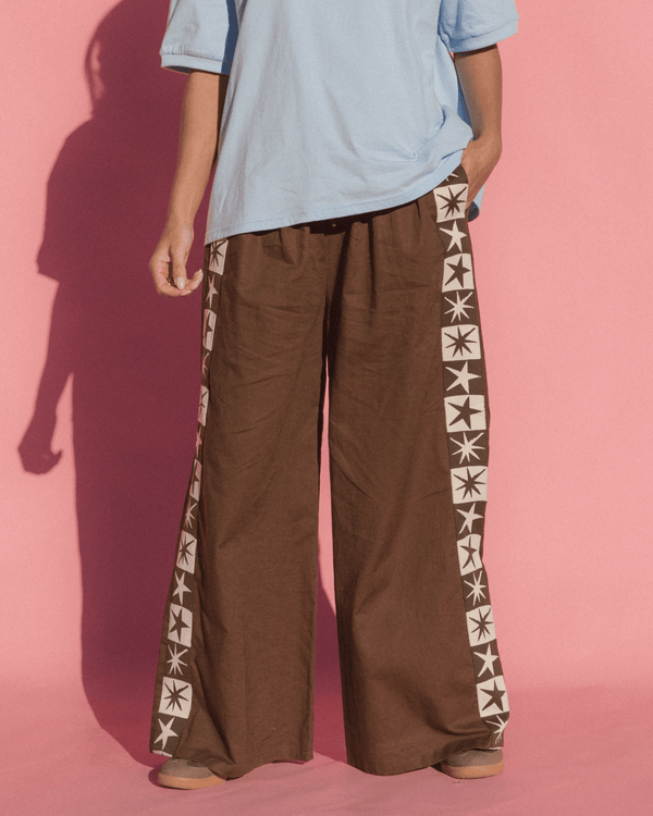 Person wearing brown wide-leg pants with star patterns on a pink background