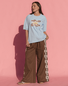 Woman wearing a light blue t-shirt and brown pants with star patterns against a pink background