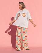 Woman wearing a white t-shirt with flower designs and colorful checkered pants on a pink background