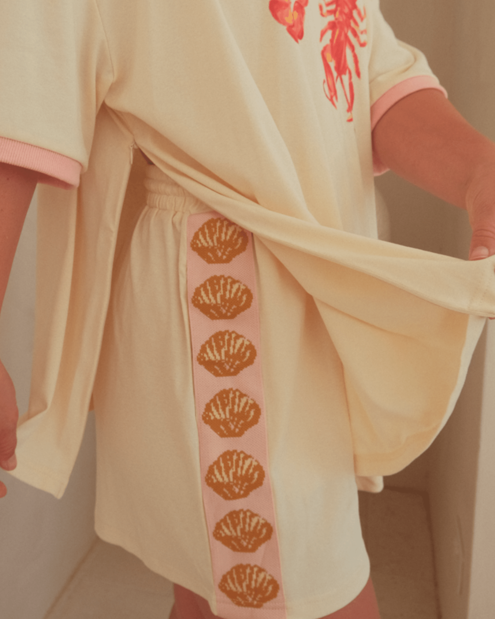 Beige outfit with pink accents and shell pattern on a neutral background. Showing breastfeeding side-zips on oversized t-shirt.